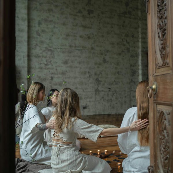 Women in peaceful meditation circle with candles inside a rustic room.